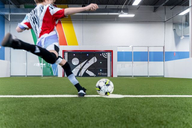 Soccer player in red, white, and black kicking a ball on an indoor turf field