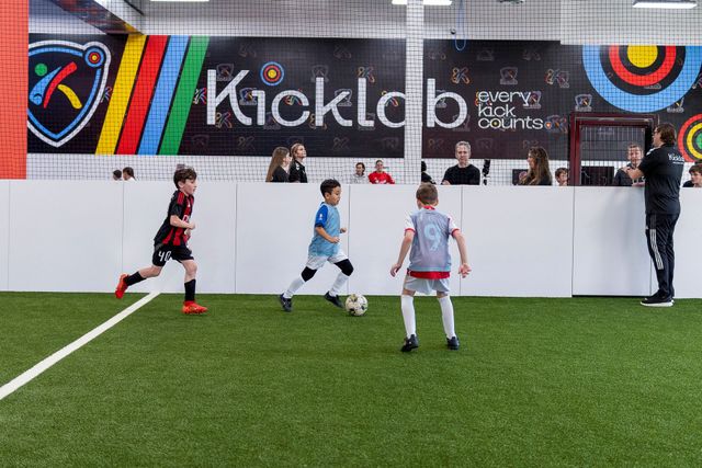 Kids playing soccer on indoor turf in front of a colorful Kick Club wall.