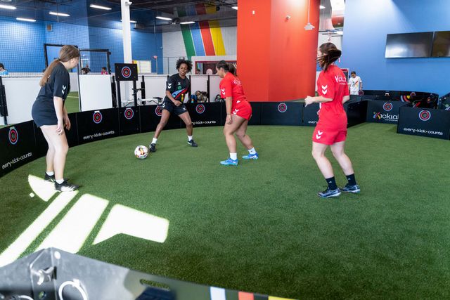 People practicing soccer indoors on artificial turf with cones and equipment around them