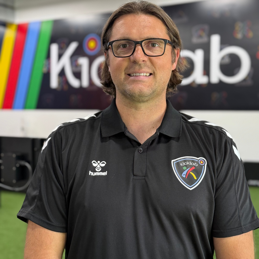 Man in black polo shirt standing in front of a colorful KidzLab sign.
