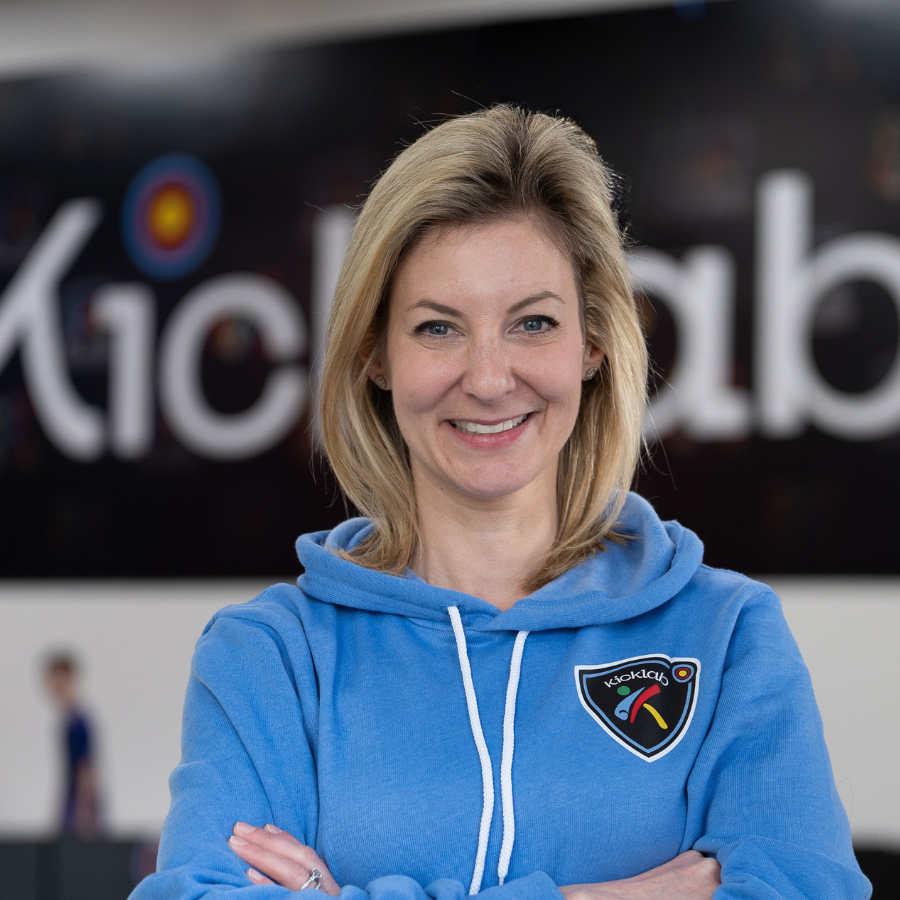 Smiling woman in a blue hoodie standing with arms crossed in a sports facility
