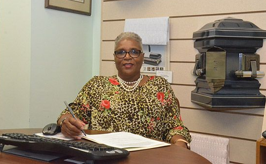 Woman sitting at a desk with papers and a phone in an office, smiling at the camera