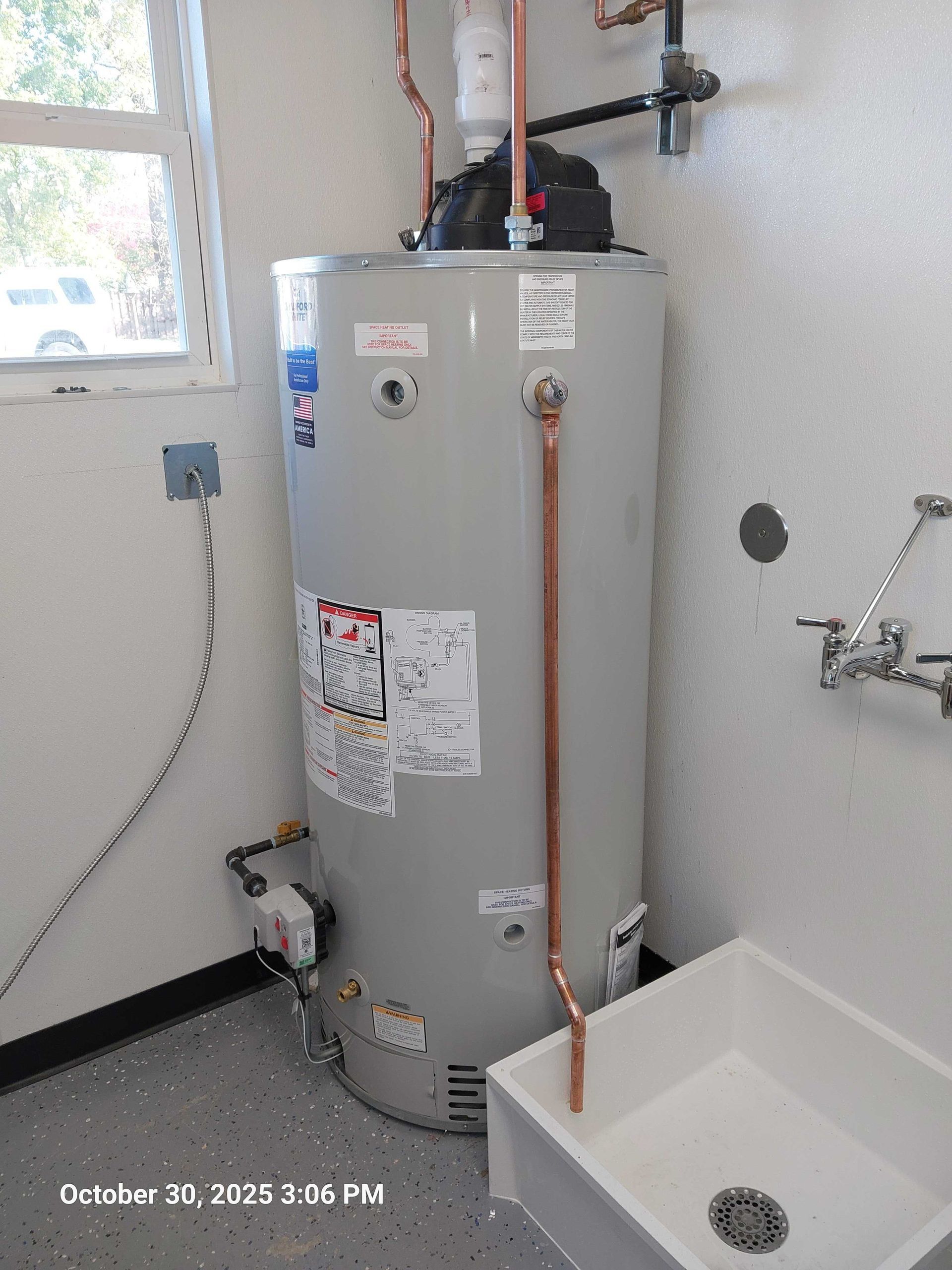 Water heater in a utility room, copper pipes, a sink, and a window.
