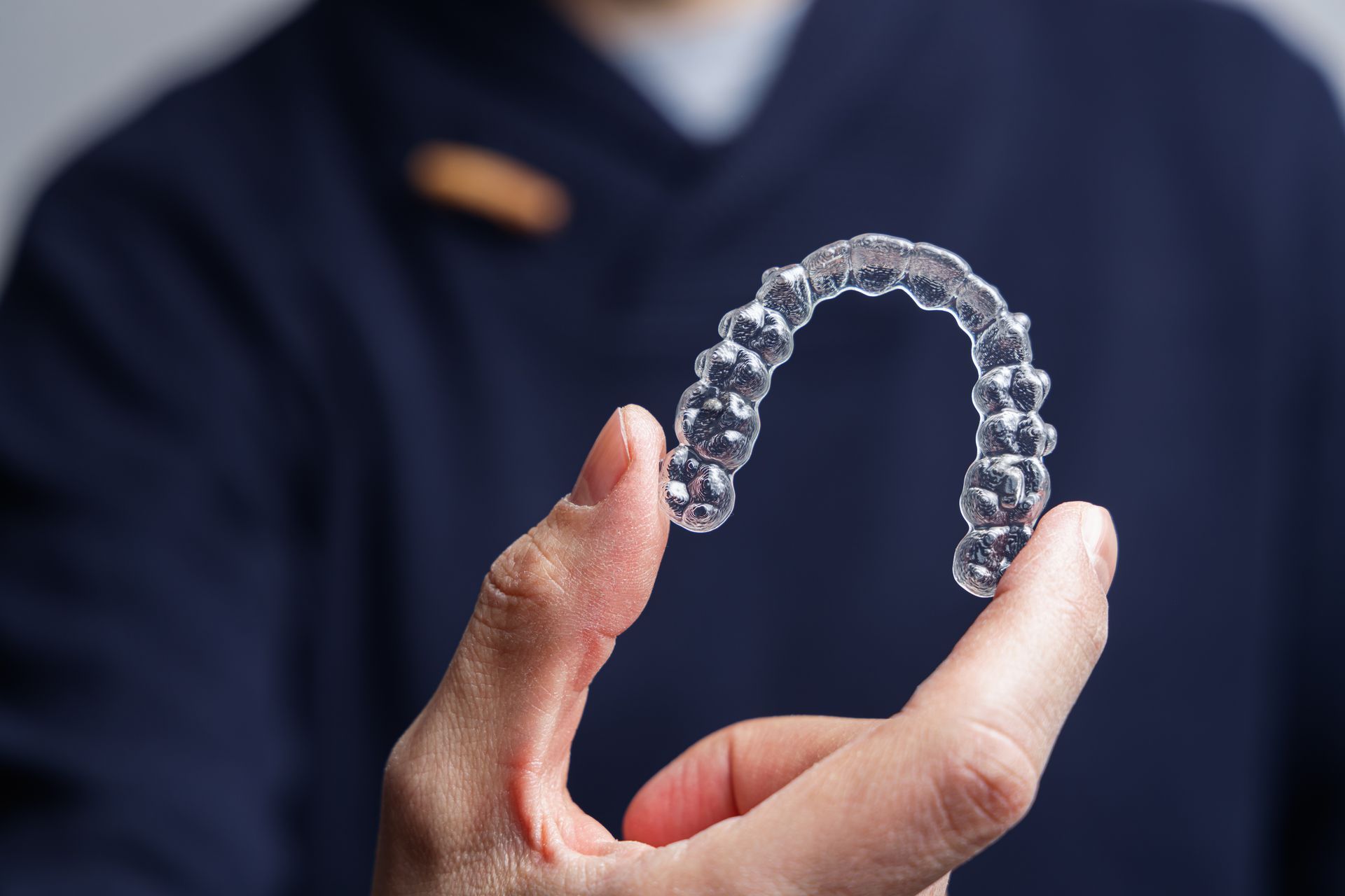 Clear dental aligner held in a person’s hand against a dark background