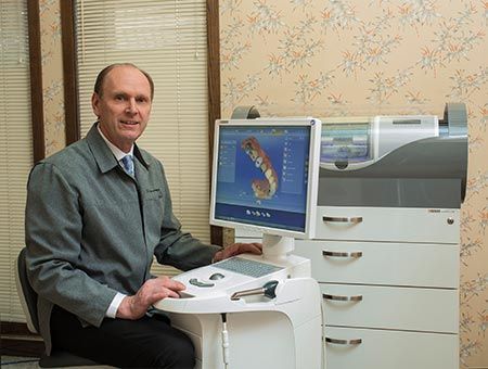 Man seated beside a large printer, working at a desktop computer in an office.