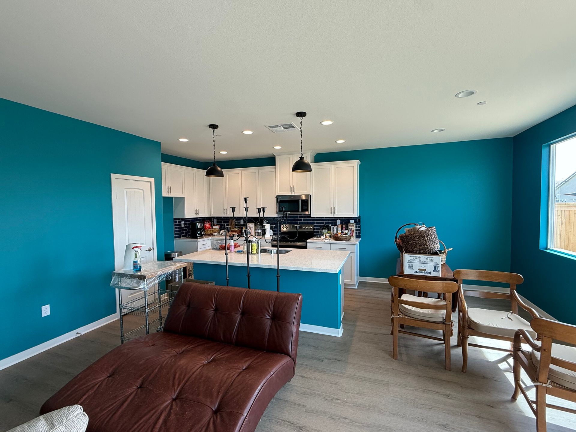 Bright living room with teal walls, brown sofa, and open kitchen in the background