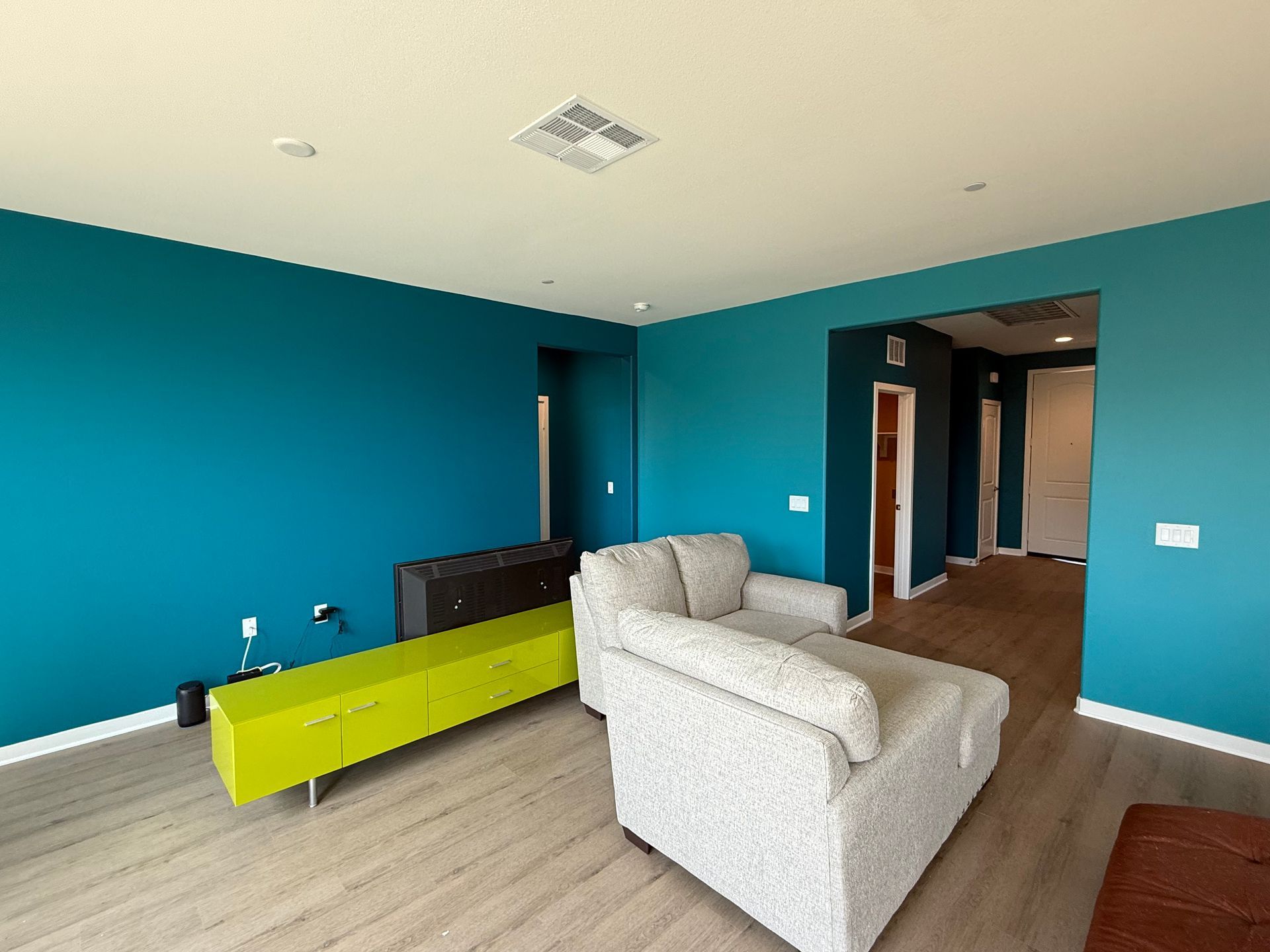 Bright teal living room with gray sofa, lime bench, and hardwood floor leading to a hallway