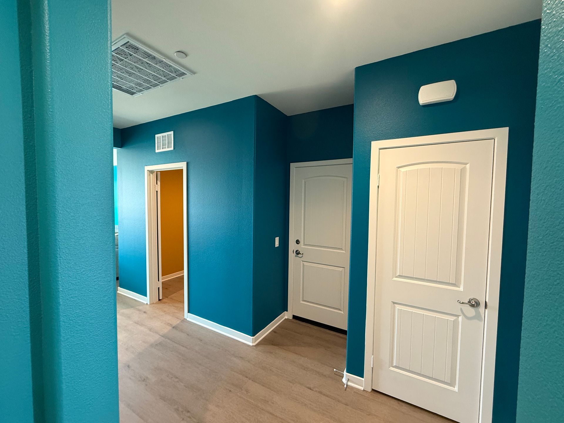 Blue hallway with three white doors, wood floor, and an open doorway at the far end