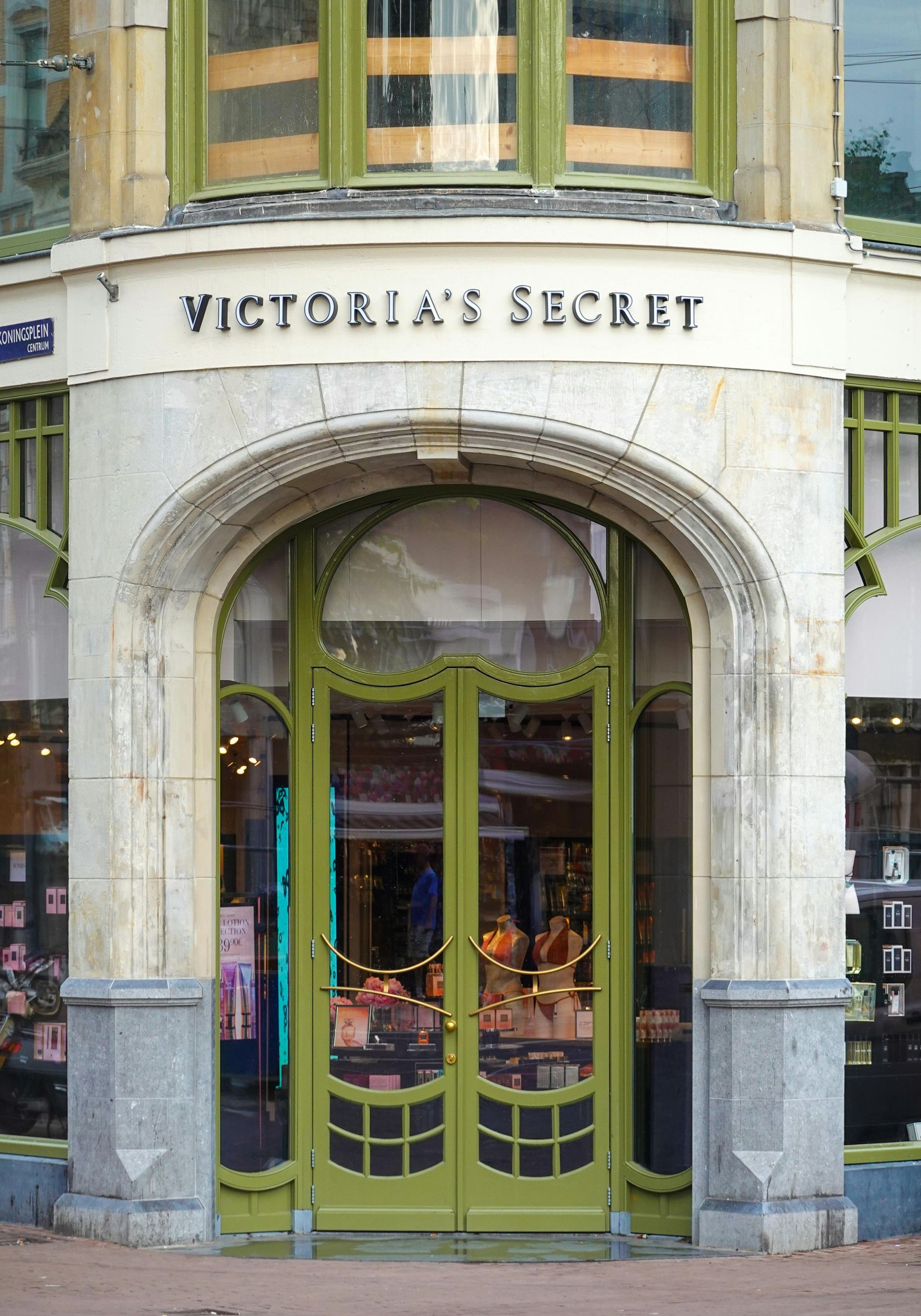 The entrance to a Victoria's Secret store featuring an ornate, arched green doorway set in a stone facade.