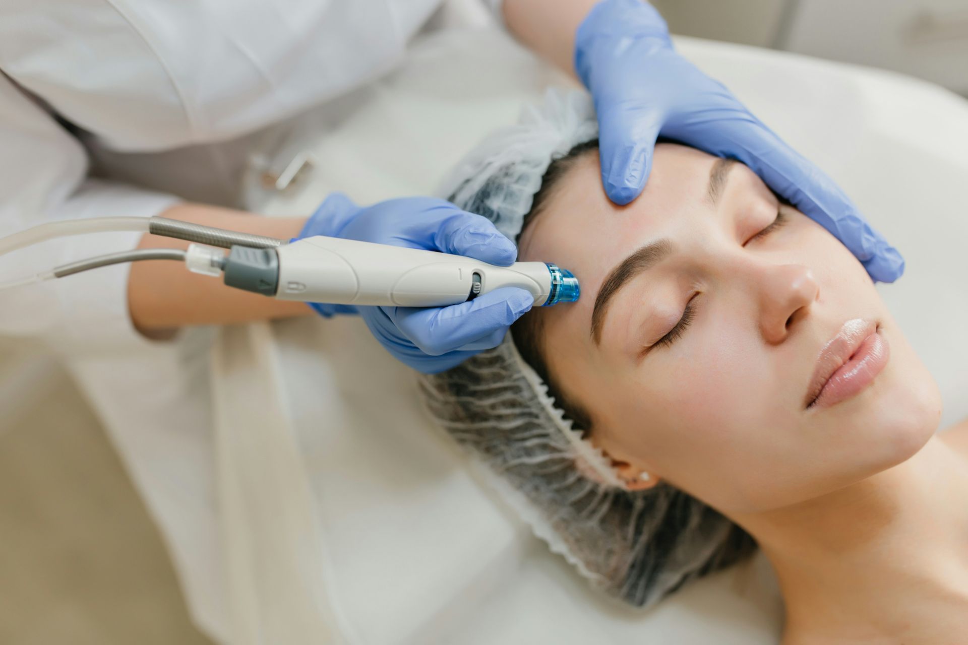 Woman receiving a facial treatment at a spa. The technician holds a device to her face.