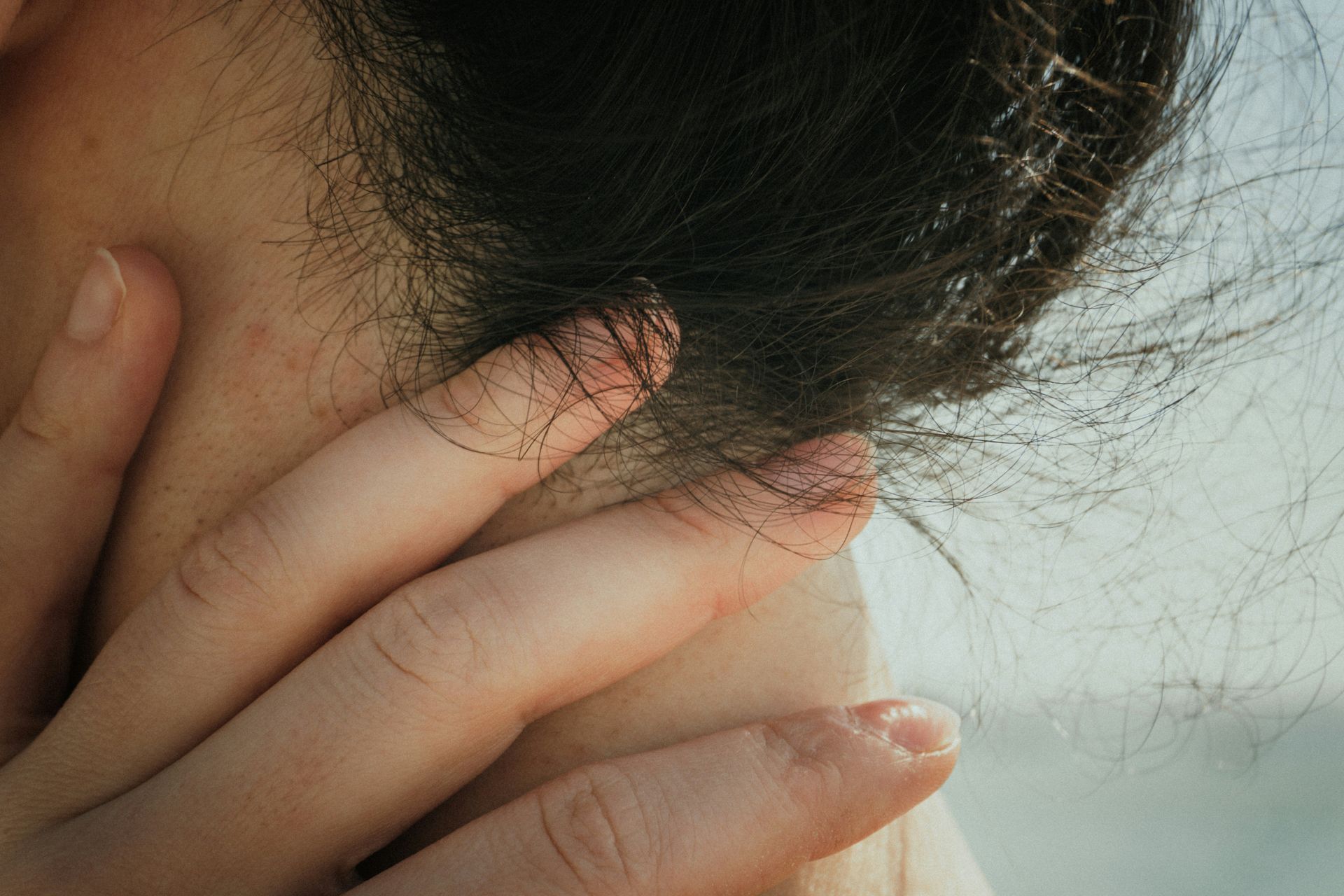 Hand touching nape of neck with dark hair, soft light.