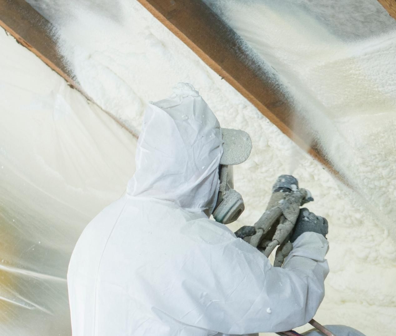A man is spraying insulation on the ceiling of a building. A man is spraying insulation on the ceiling of a building.