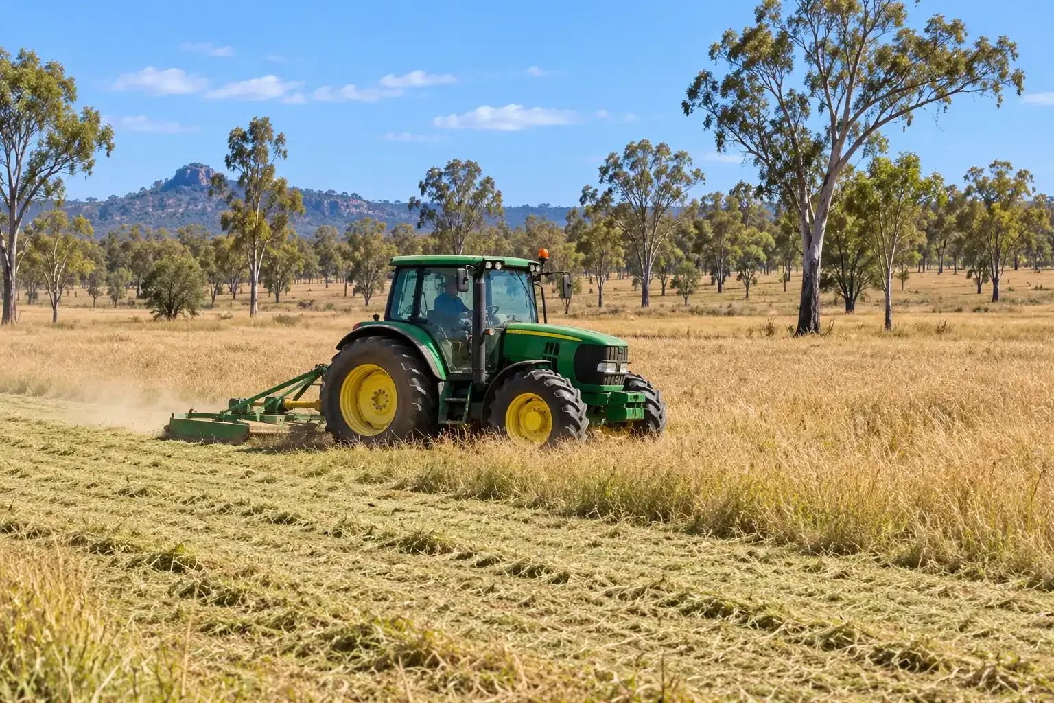 Right-side view of a green John Deere Tractor slashing an open rural paddock in the Townsville region.