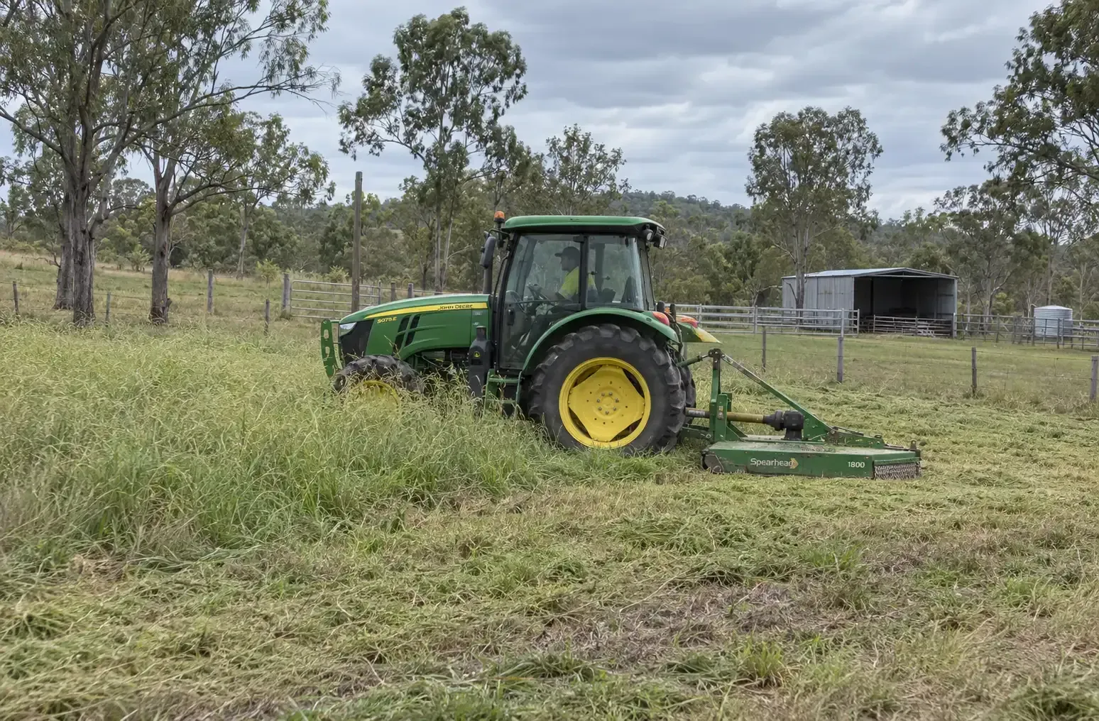 Left-side view of a green tractor and slasher combo mowing an overgrown paddock in rural Townsville.