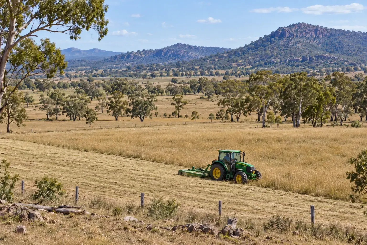 Green tractor with rear mounted slasher working in a large paddock near Townsville, QLD