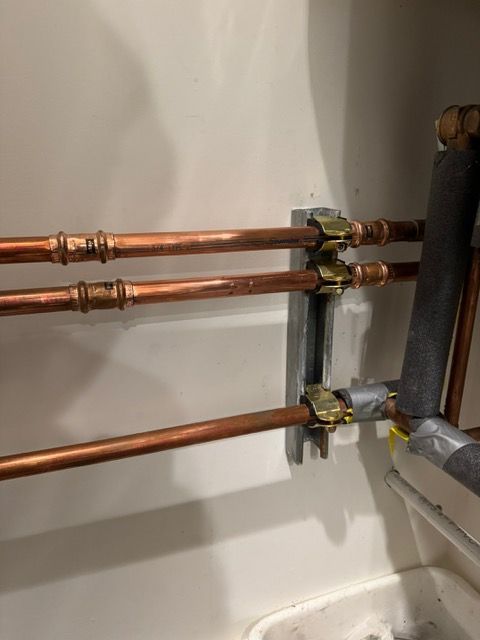 Three copper pipes are connected to each other on a wall.