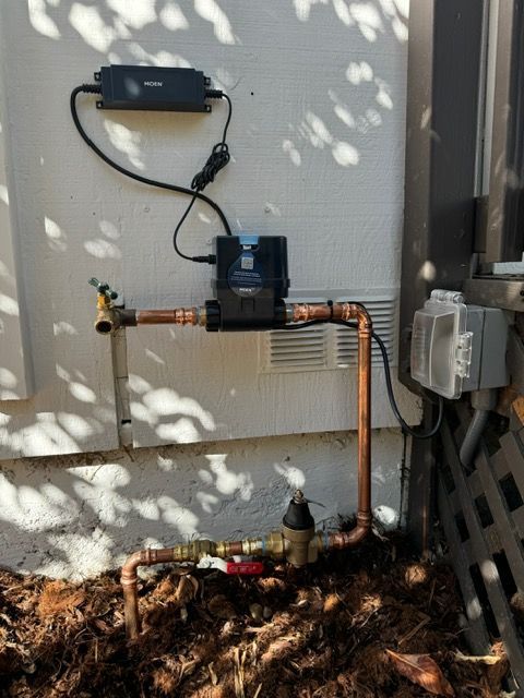 A water meter is attached to a copper pipe on the side of a building