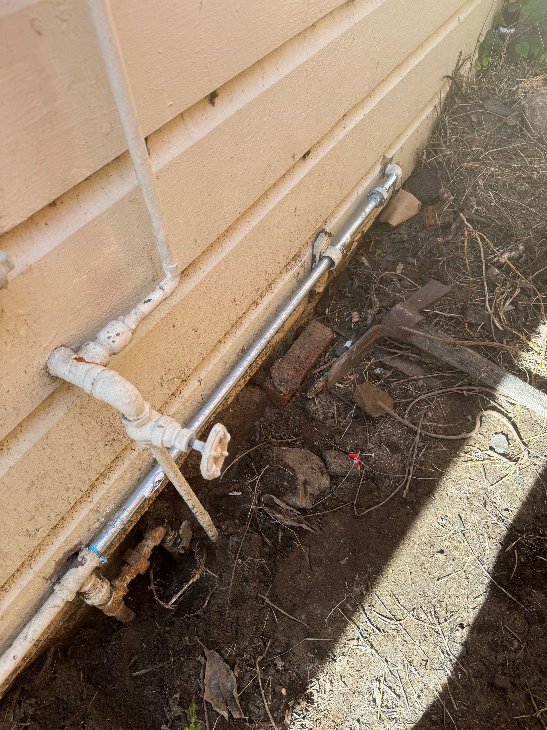 A pipe is laying in the dirt next to a house.