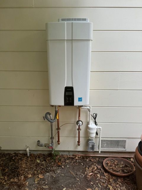 A white water heater is mounted on the side of a house.