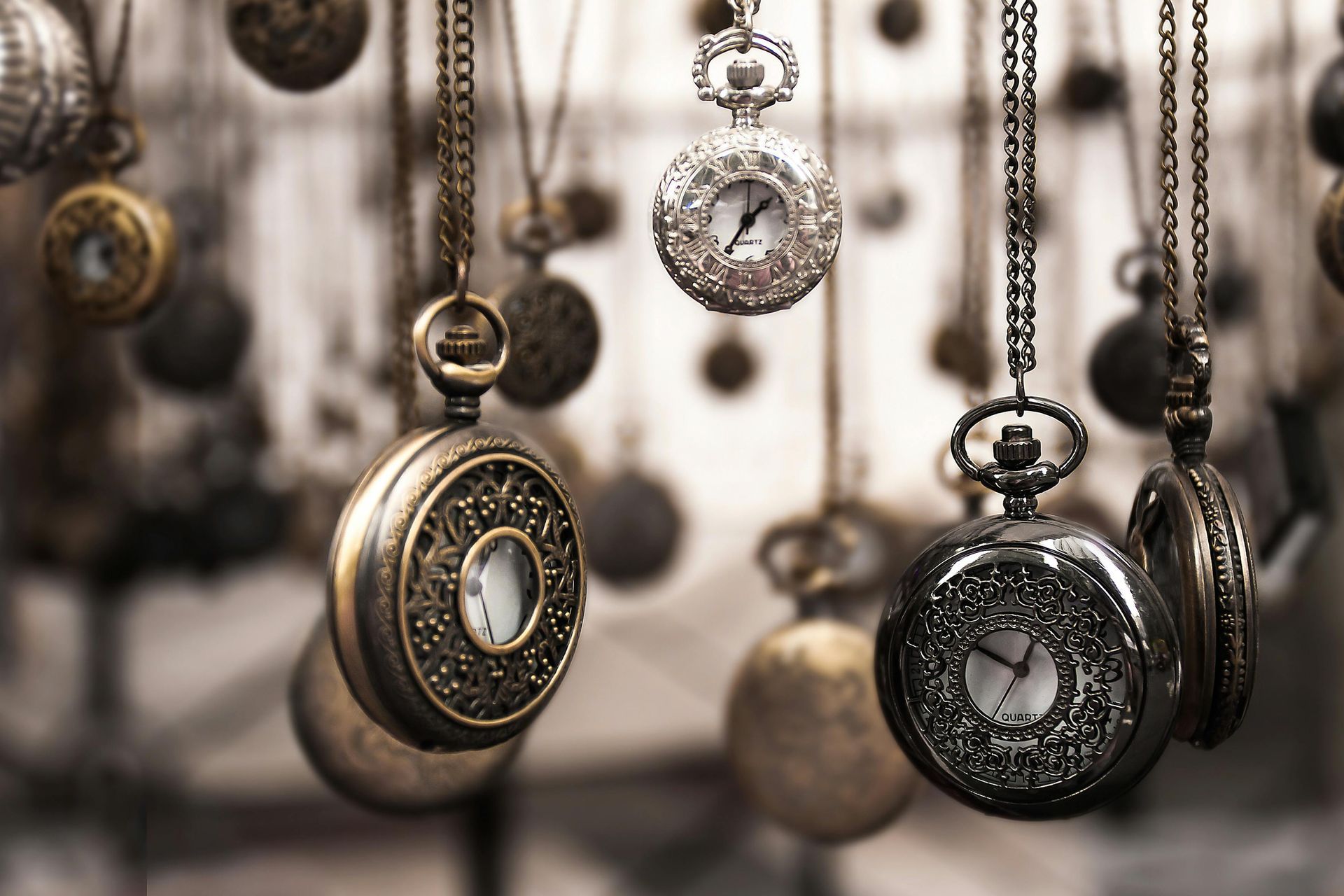 Vintage pocket watches hanging on chains, in silver, gold, and black tones.
