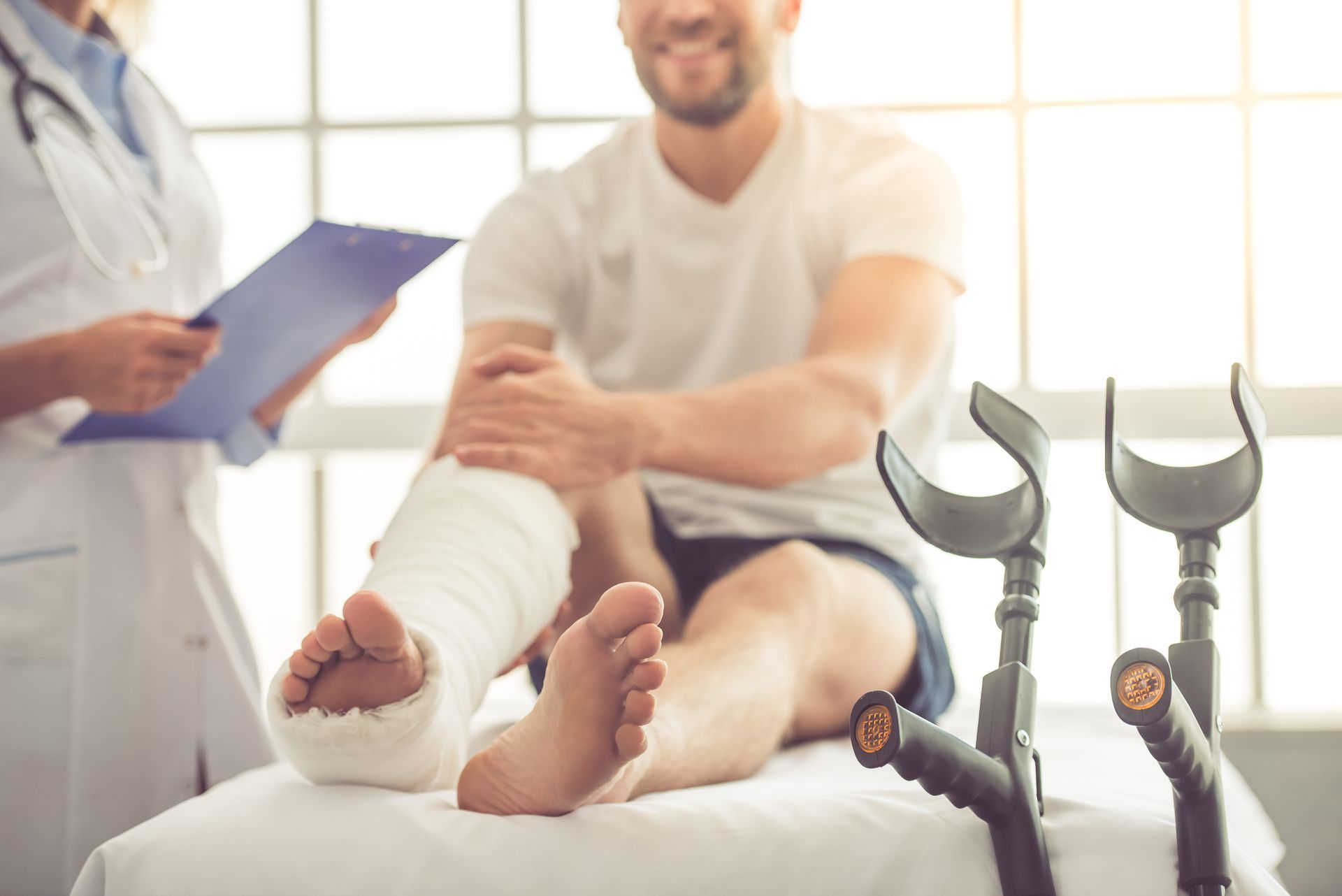 Doctor examining male patient with broken leg cast and crutches at medical clinic. Doctor examining male patient with broken leg cast and crutches at medical clinic.