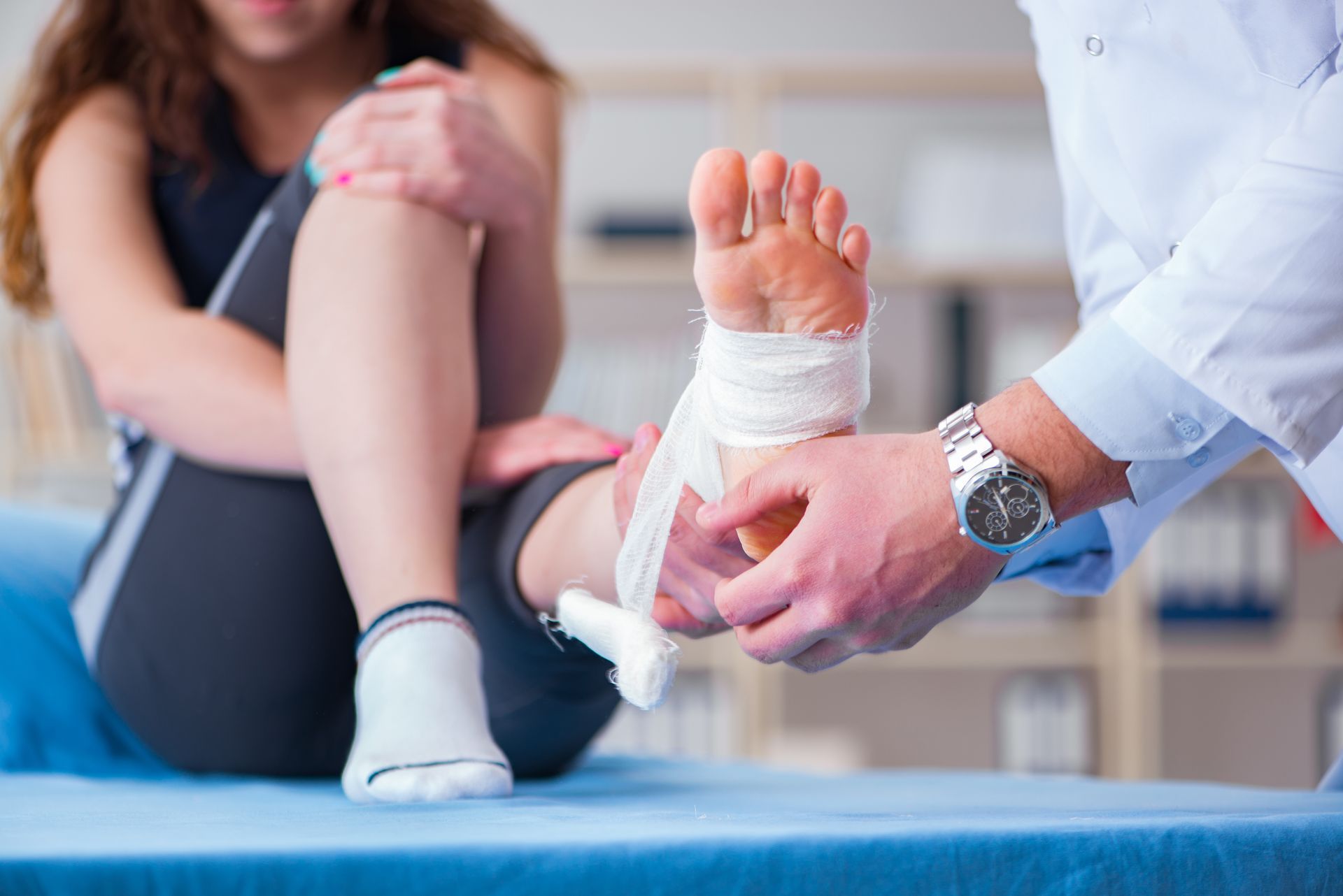 Sports injury doctor wrapping ankle bandage for athlete with foot injury on exam table. Sports injury doctor wrapping ankle bandage for athlete with foot injury on exam table.
