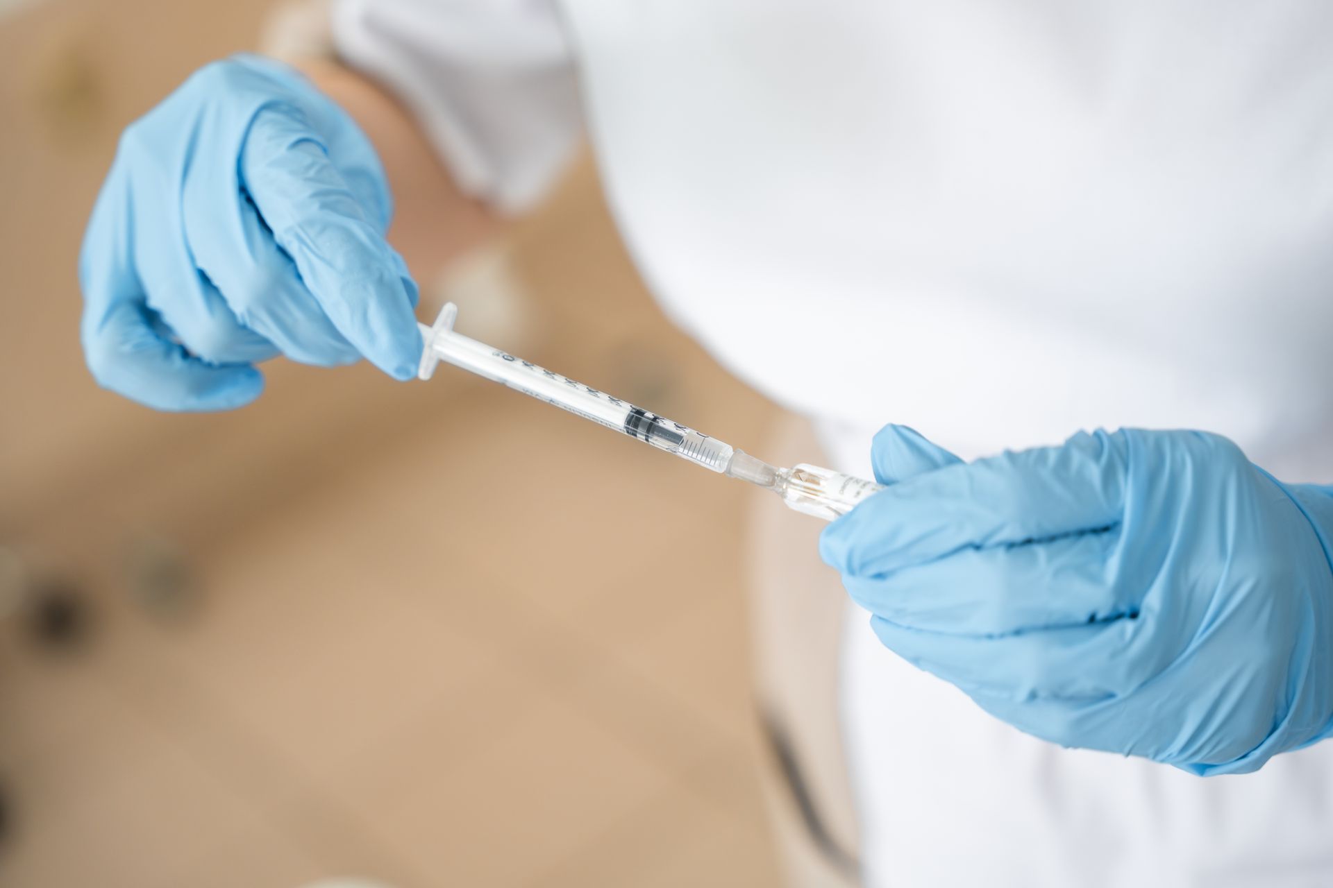 Close-up of a doctor's hand filling a vaccine syringe before injection. Close-up of a doctor's hand filling a vaccine syringe before injection.