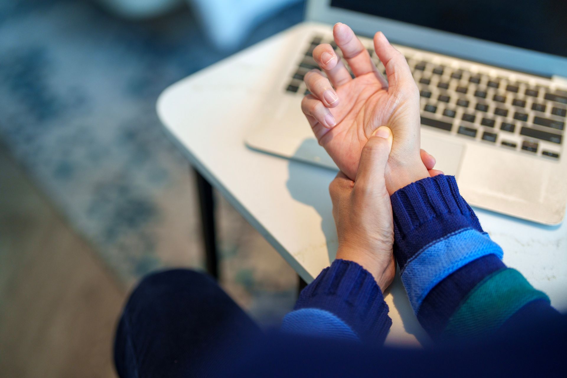 Woman massaging her hand, showing wrist pain from arthritis after extended computer use.