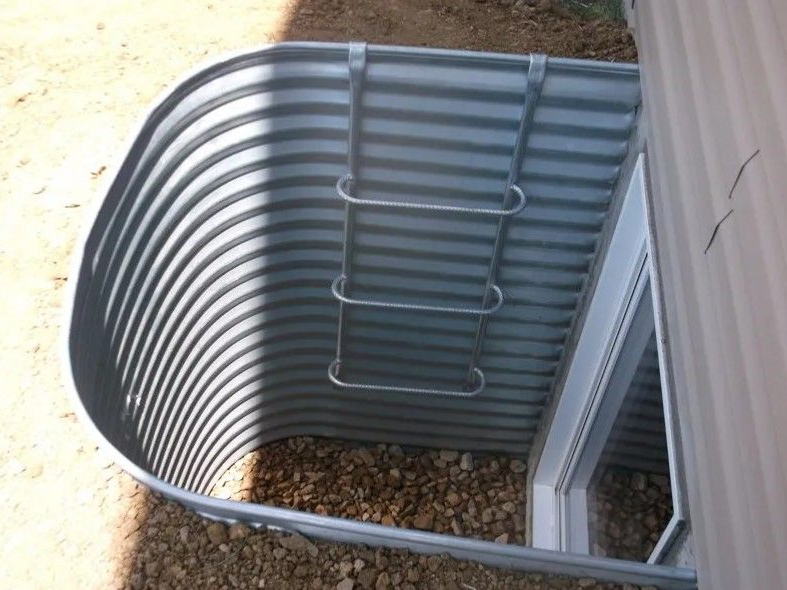 Metal window well with ladder and gravel, next to a building with a visible window.