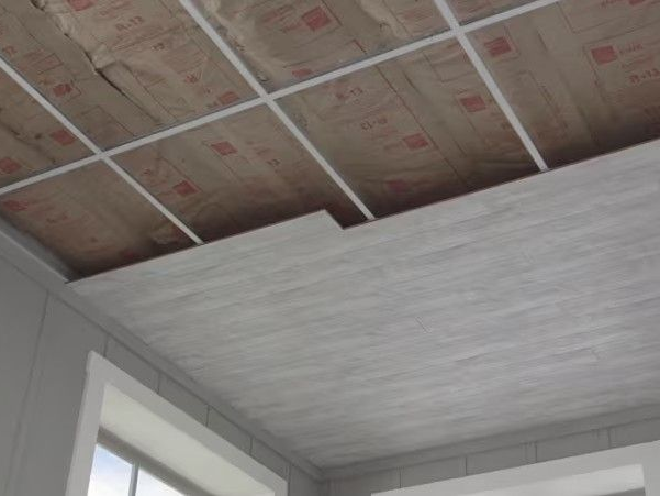 Partial view of a suspended ceiling being installed, showing insulation, metal grid, and panel placement.
