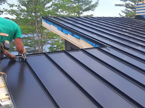 Person installing black metal roof panels on a building.