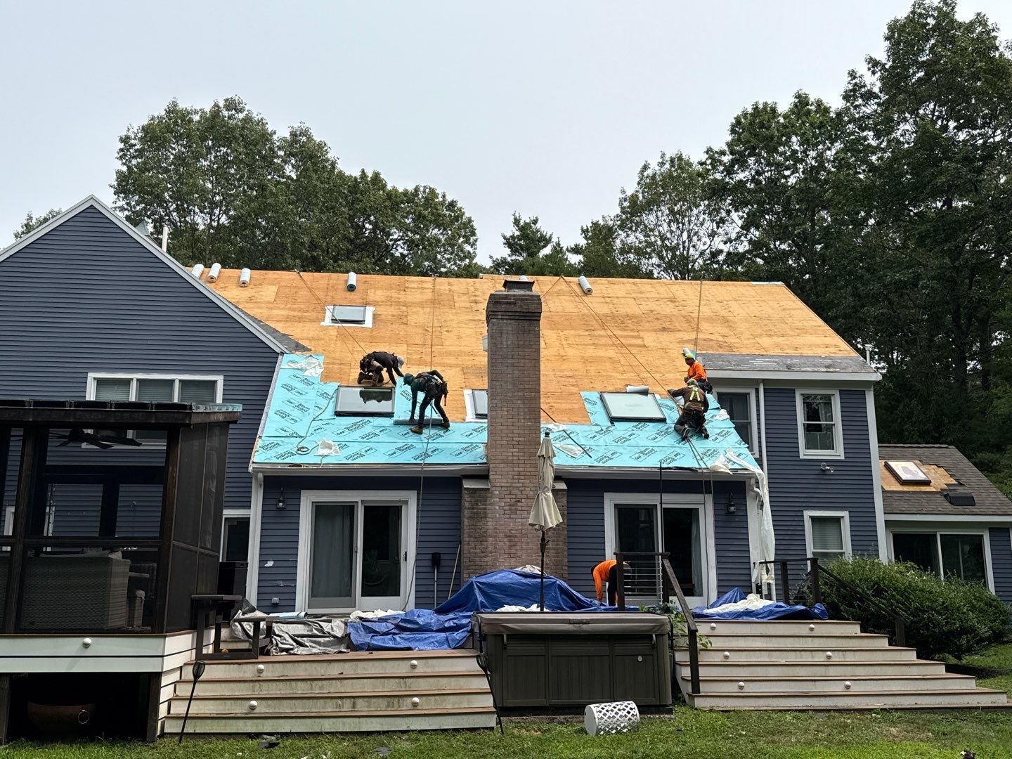Roofers working on a house, removing old shingles and installing new ones; the house is blue.