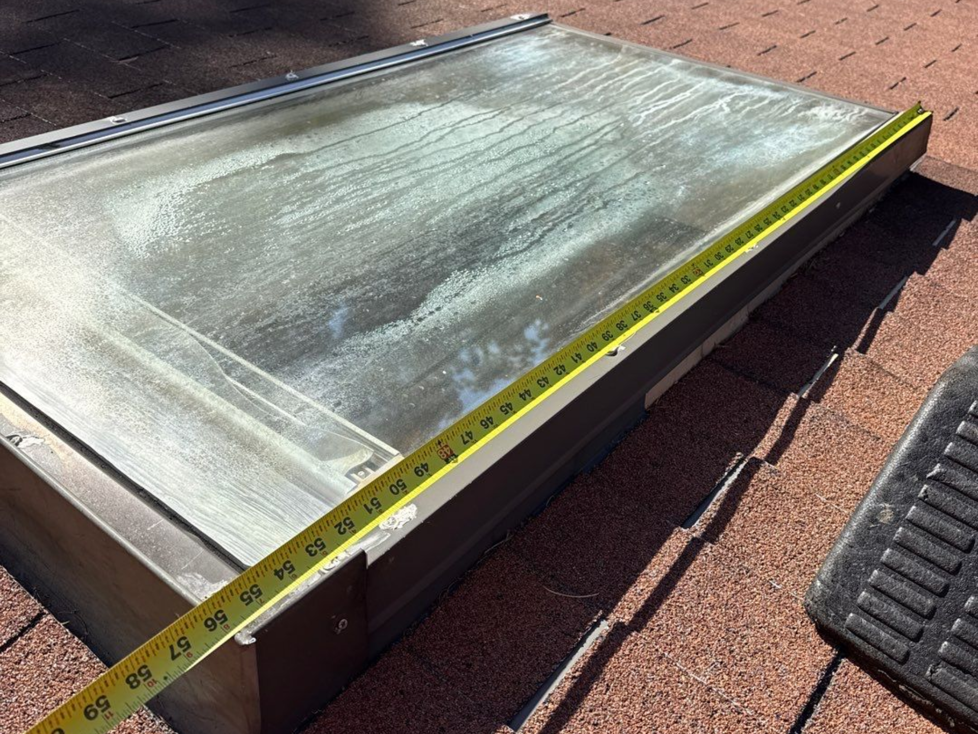 Skylight on a rooftop being measured with a yellow tape measure.