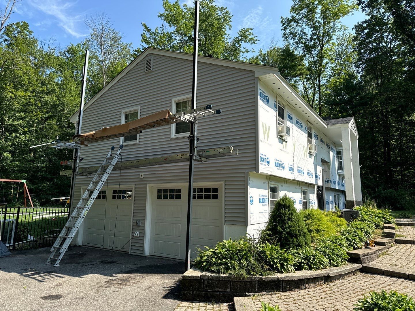 Two-story house with gray siding under renovation; scaffolding and ladder visible.