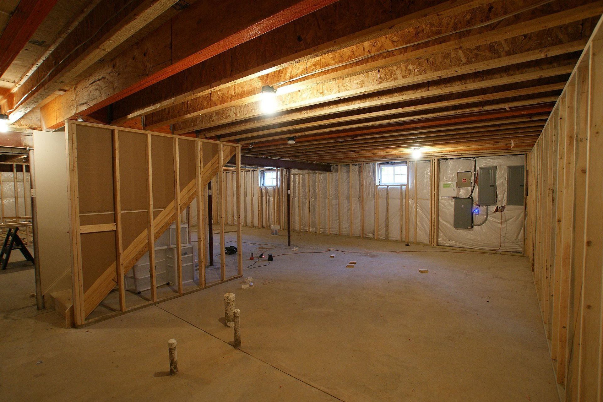 Basement interior showing a black pipe, concrete floor with water, and wooden framing.