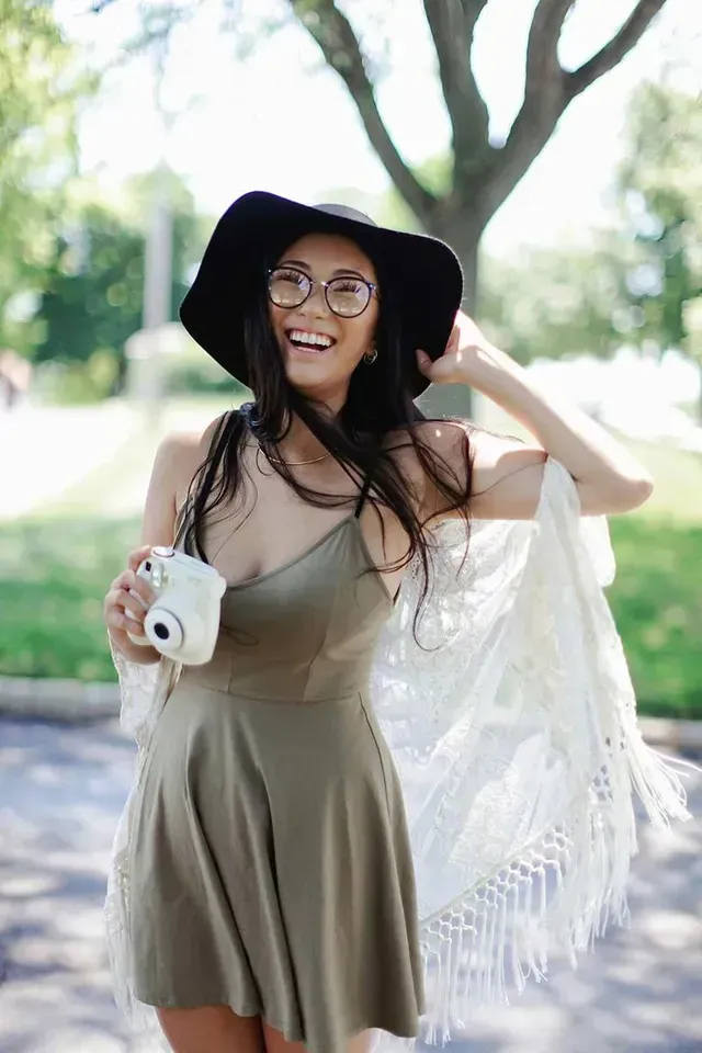 A woman in a green dress is holding a camera and smiling.