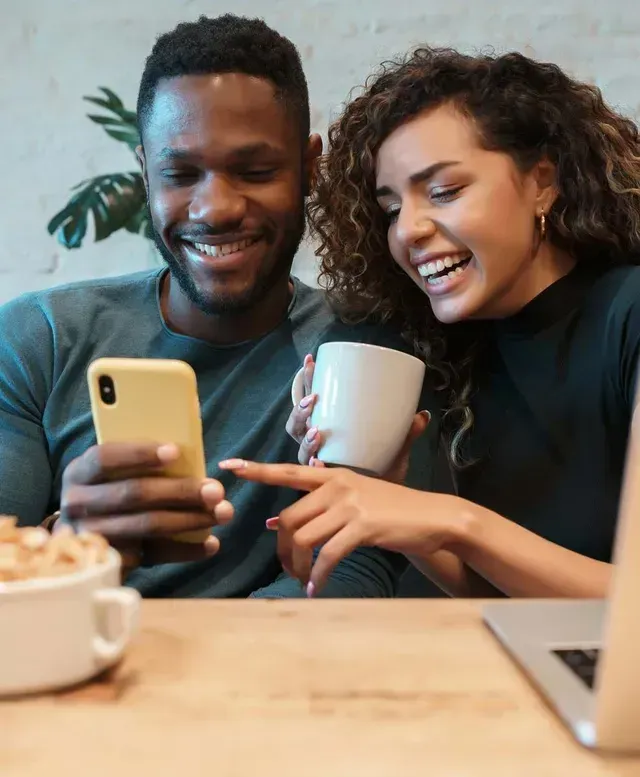 A man and a woman are sitting at a table looking at a cell phone