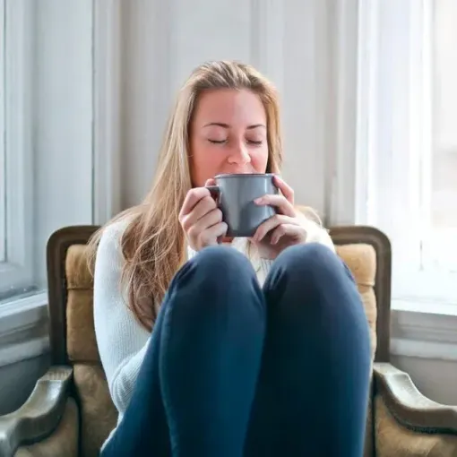A woman is sitting in a chair drinking from a cup.