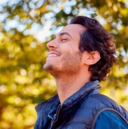 A man in a vest is smiling and looking up at the sky.