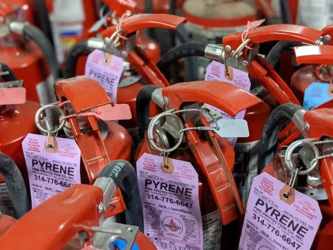 Red fire extinguishers with orange handles and tags stacked together in a close-up view