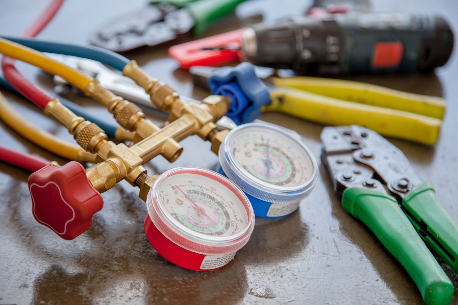 HVAC gauges, hoses, and tools on a reflective surface; red, blue, yellow, and green.