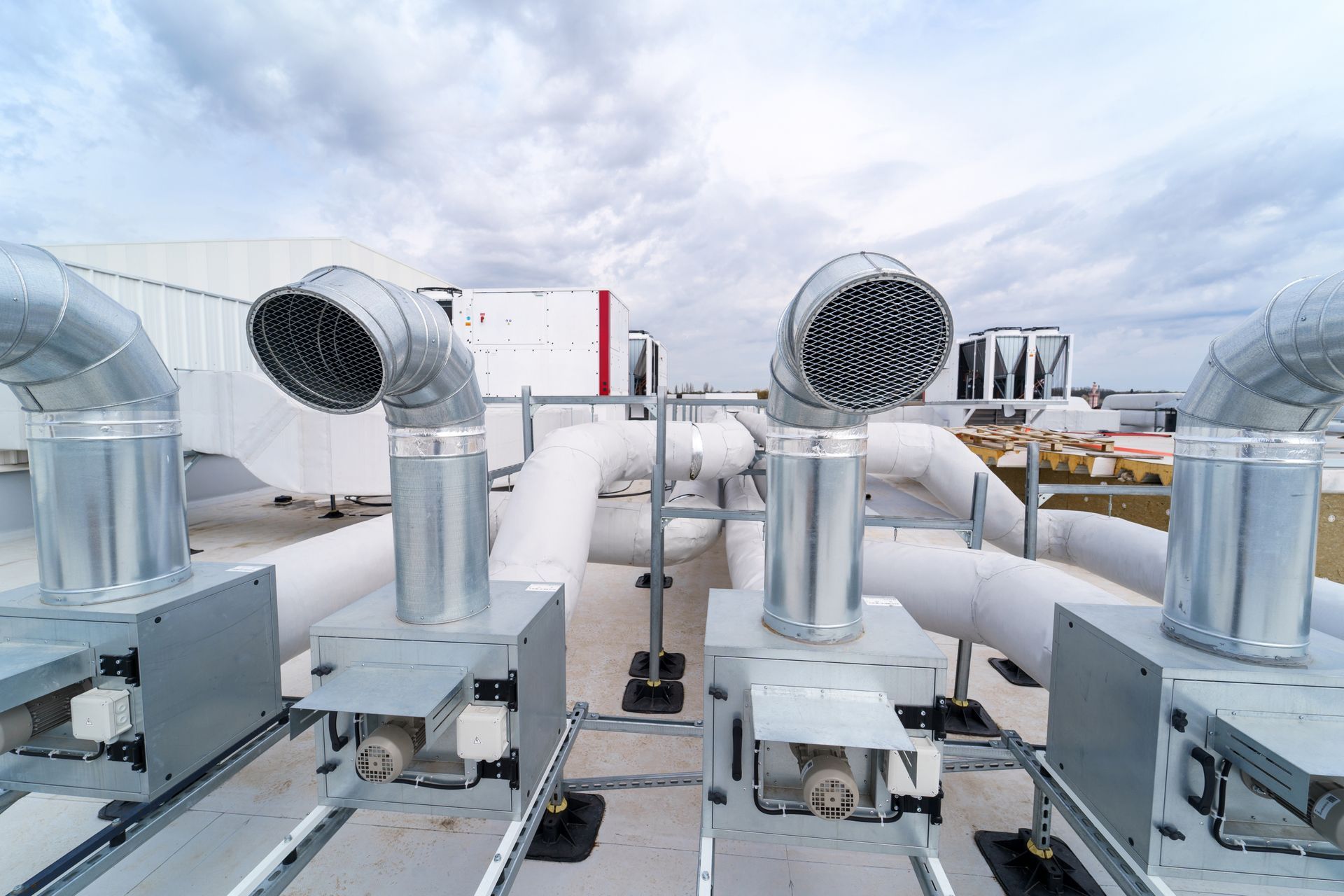 Rooftop HVAC system with silver vents and pipes against a cloudy sky.