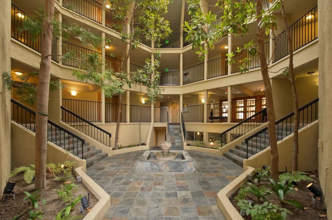 Courtyard with multiple levels, trees, stone flooring, stairs, and balconies in neutral tones.