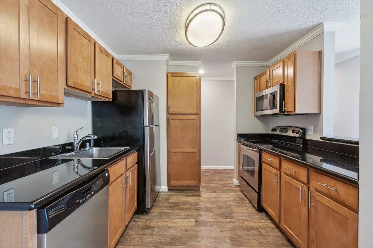 Kitchen with wood cabinets, black countertops, stainless steel appliances, and wooden floor.
