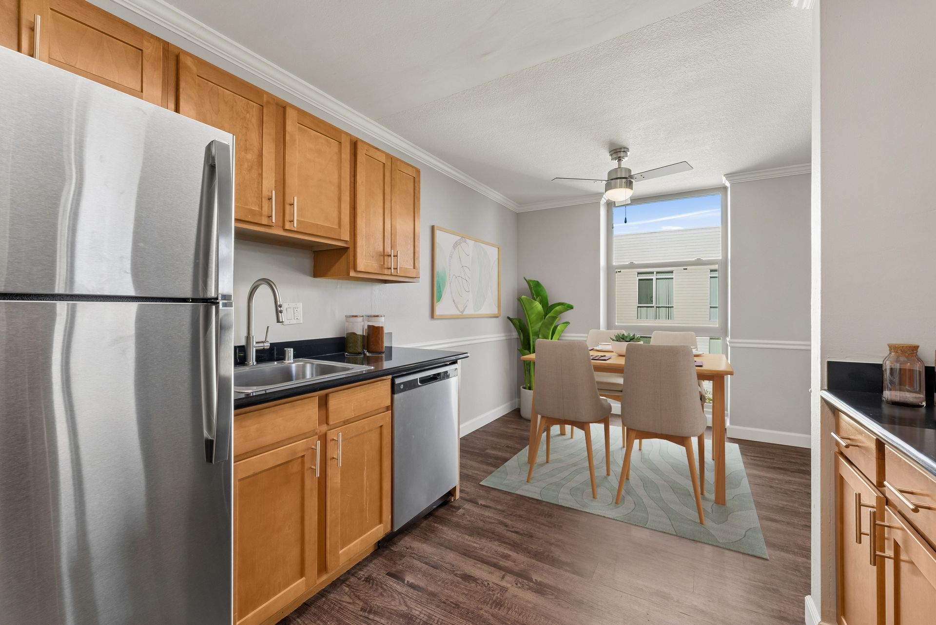 Bright kitchen with stainless steel fridge, wood cabinets, and a dining table by a window.