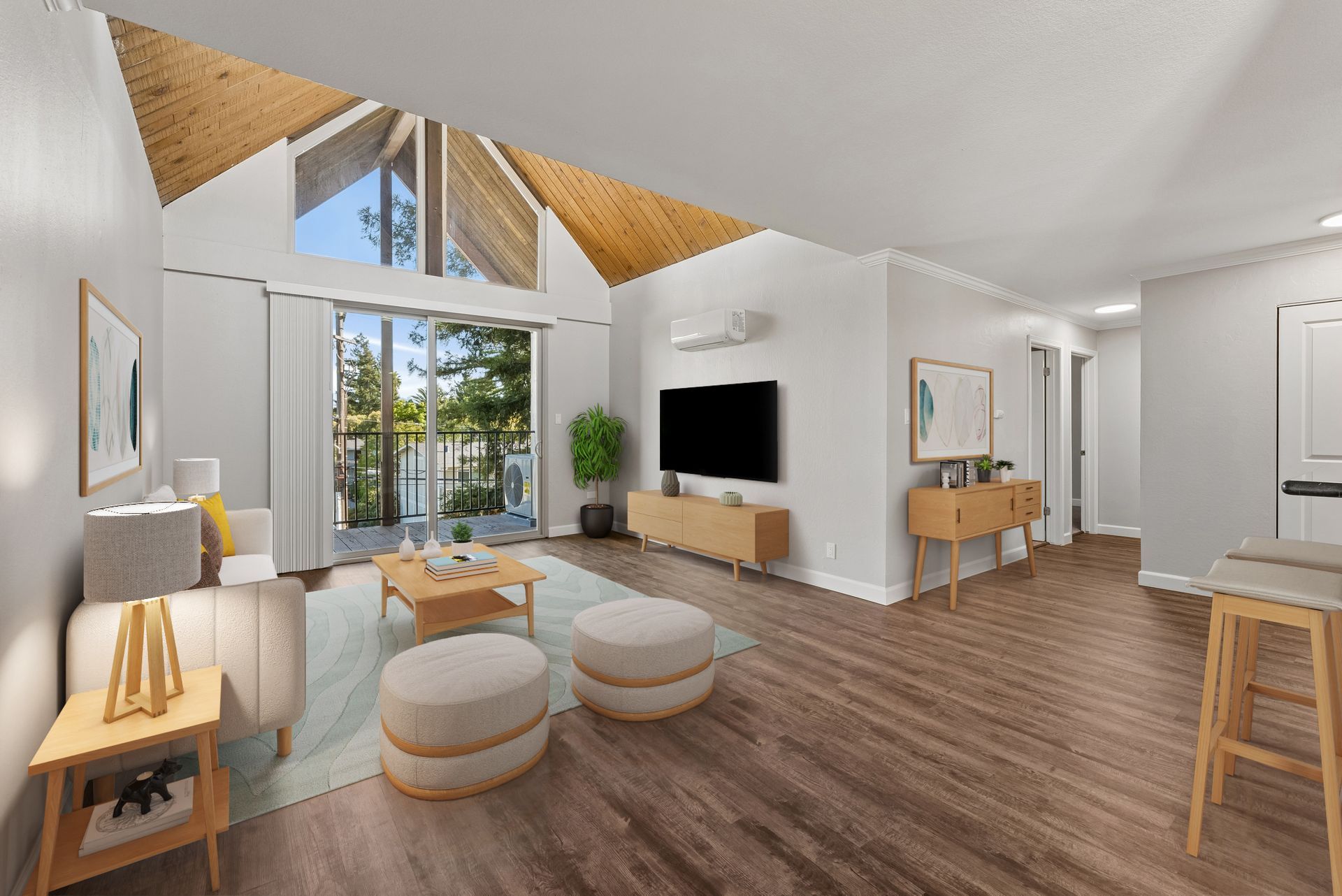 Bright modern living room with vaulted wood ceiling, large windows, TV, and light wood furniture