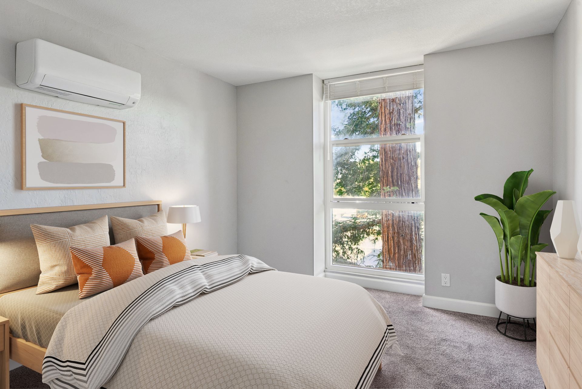 Bright bedroom with a bed, framed art, potted plant, and window letting in natural light