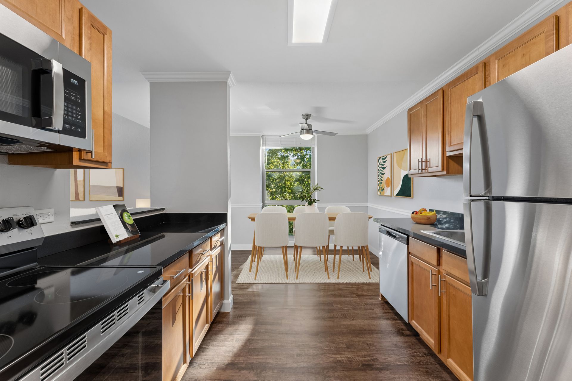 Bright modern kitchen with wood cabinets, stainless appliances, black countertops, and a dining table by a window
