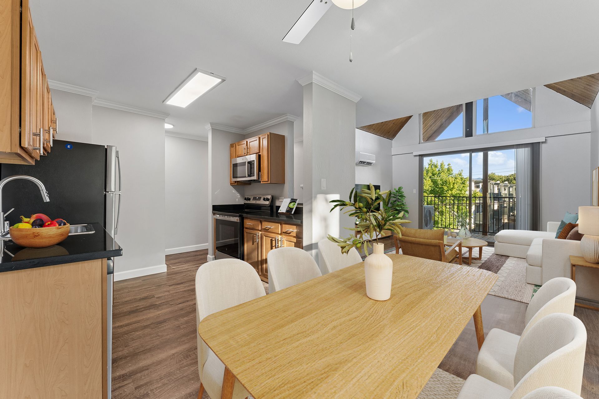 Bright modern dining and living room with a wooden table, white chairs, and large windows overlooking greenery