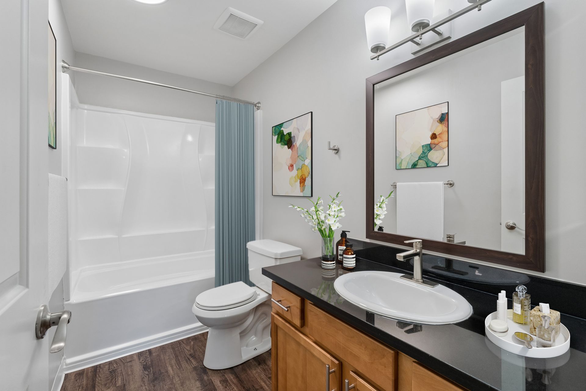 Modern bathroom with white tub, toilet, wood vanity, large mirror, and gray shower curtain